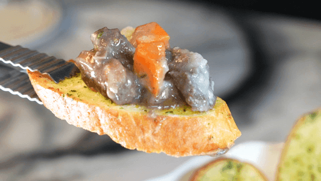 Tongs holding garlic bread topped with beef stew