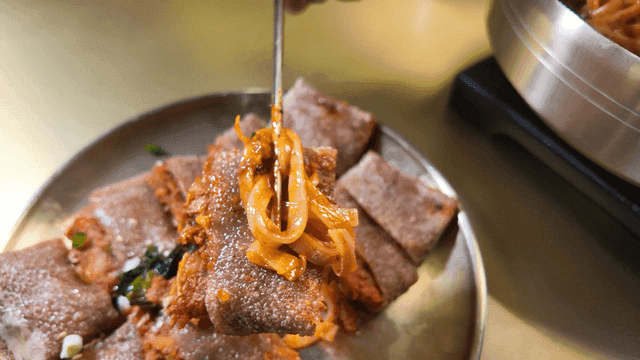 Chopsticks holding bibim kalguksu on buckwheat pancake