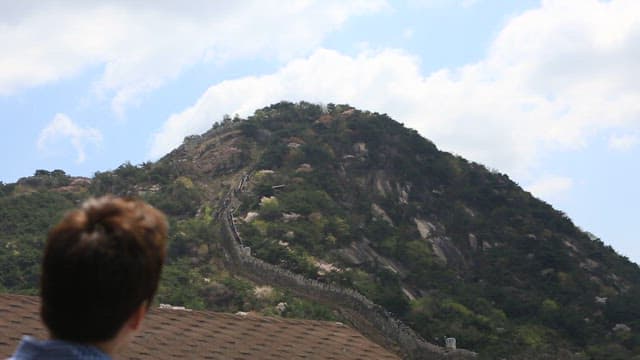 성곽길과 주택이 있는 산악 경관을 손가락으로 가리키는 사람