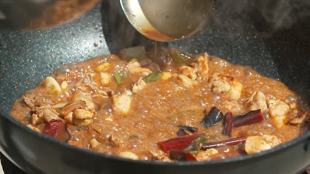 Stir-frying chili peppers and meat in a large wok with sauce