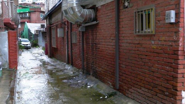 Rain-soaked narrow alley with wet pavement and parked car