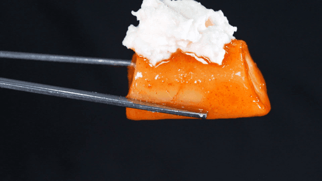 Chopsticks holding tteokbokki topped with spicy sauce and potato salad