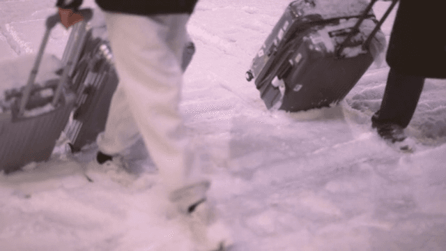 People walking along snow-covered streets, dragging their luggage