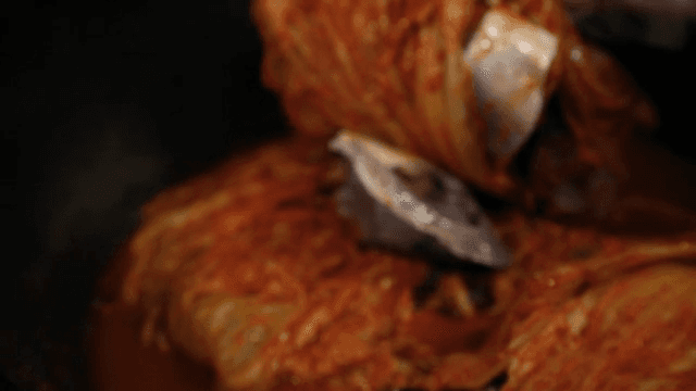 Kimchi being mixed with fish in a pot