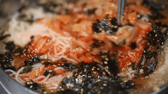 Kimchi-wrapped noodles being stirred with chopsticks
