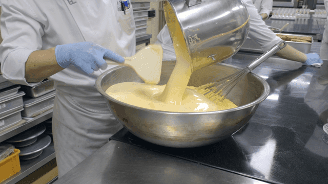 Baker pouring batter into mixing bowl
